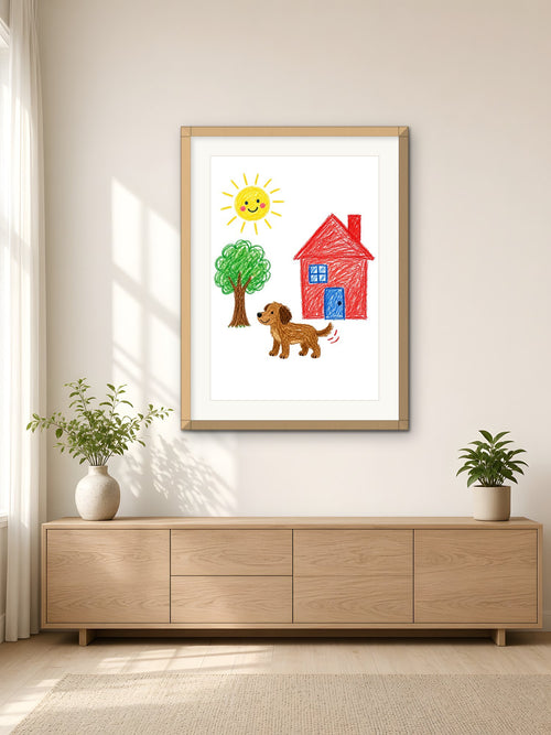 A child's crayon drawing of a sun, tree, red house and brown dog, framed in light oak on a bright living-room wall